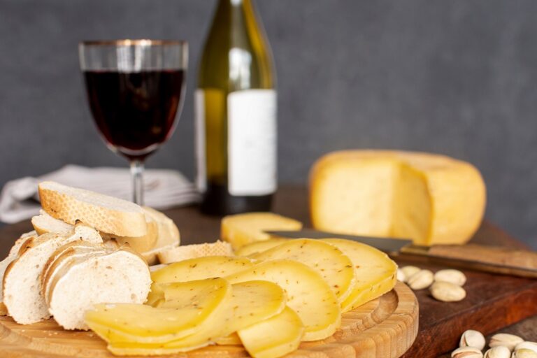 Cheese board with bottle of wine and glass of wine in the background.