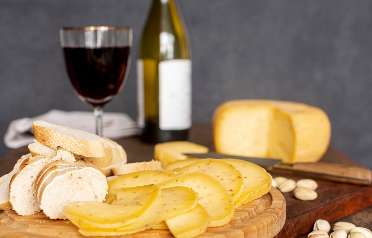 Cheese board with bottle of wine and glass of wine in the background.