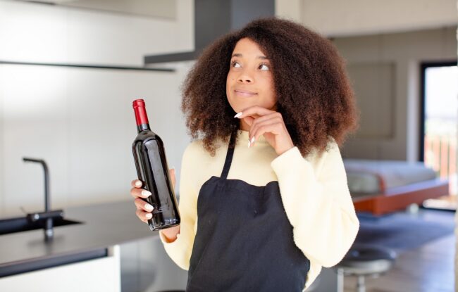Woman in kitchen holding bottle of wine illustrates blog "Is Cabernet Sauvignon a Dry Wine?"