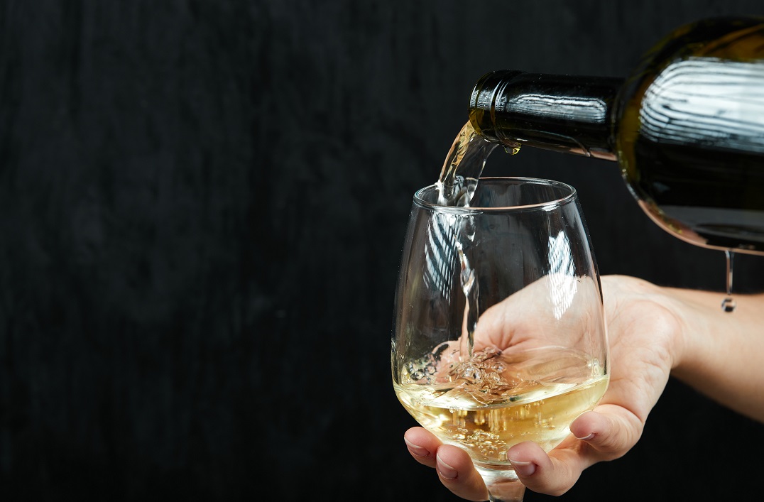 Closeup of hands pouring white wine in glass.