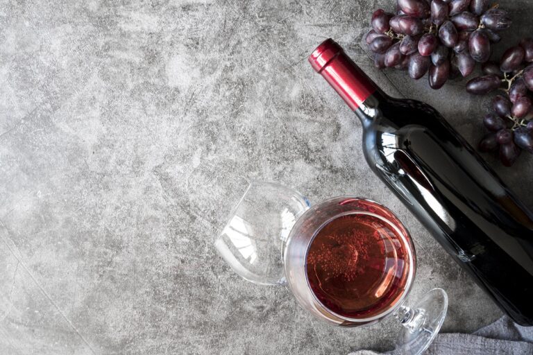Grapes, bottle of red wine, and glass of wine set against gray background.