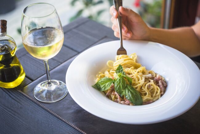 White Wine and Pasta Person holding fork with plate of pasta and glass of wine on the table.